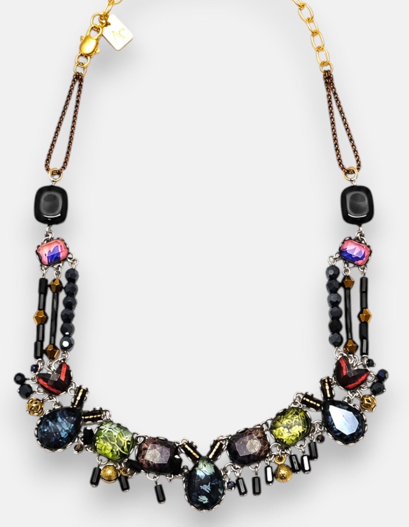 diseño del collar dispuesto de forma arqueada sobre fondo neutro, destacando la composición en mosaico con tonos verdes, violetas y azules.