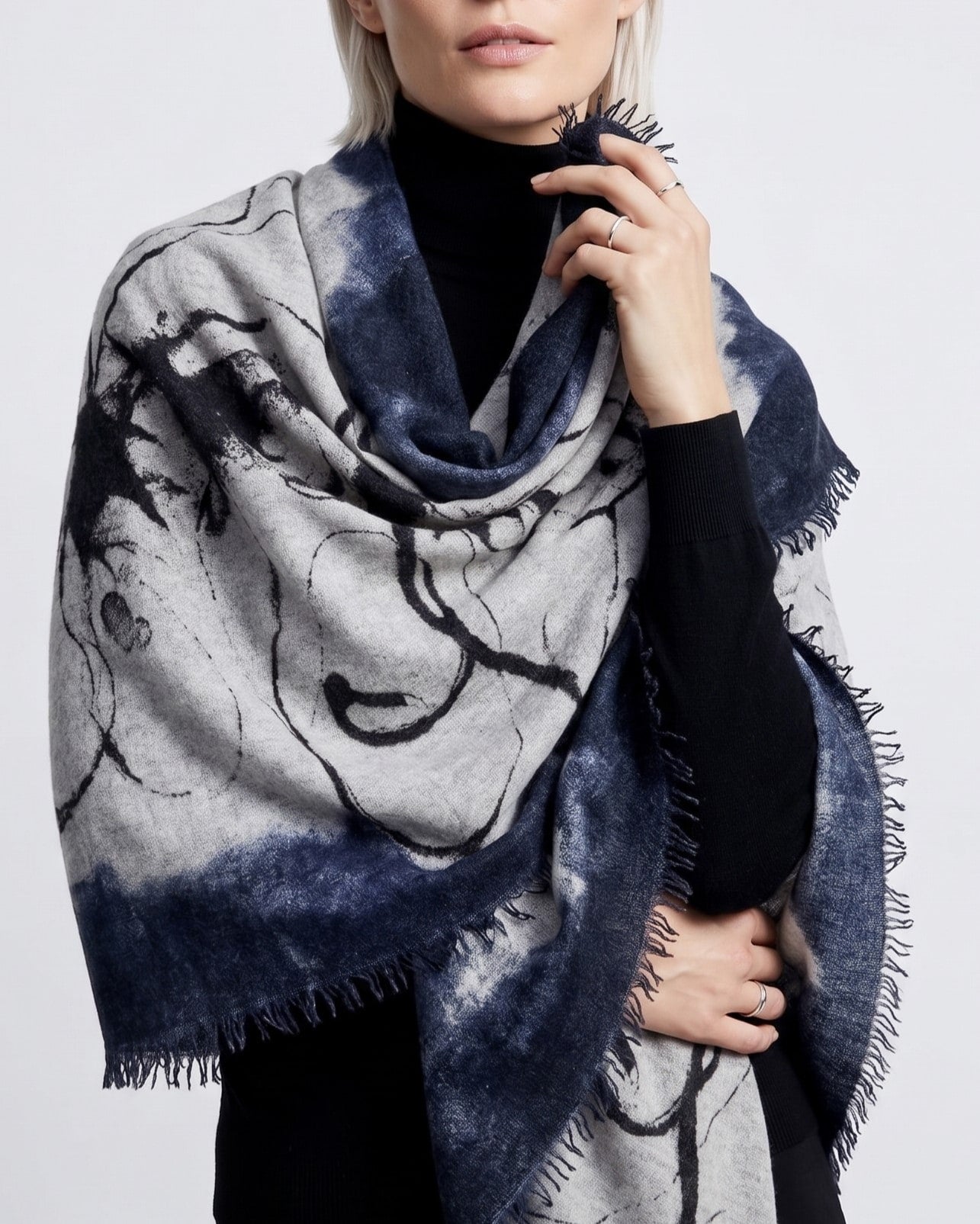Modelo luciendo el foulard de cashmere Faliero Sarti Pia drapeado sobre los hombros con fondo azul marino y gris sobre un jersey negro.