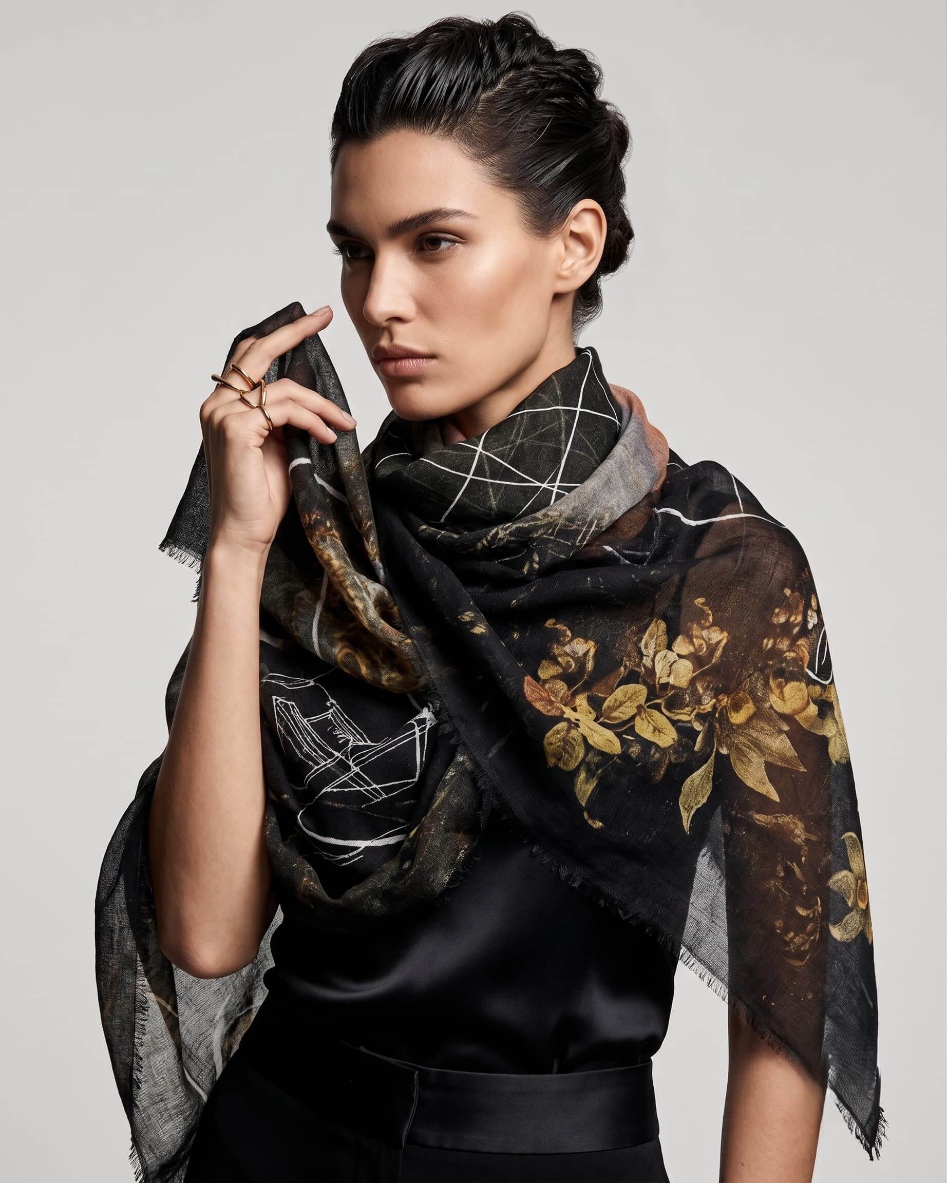 Modelo luciendo el pañuelo Faliero Sarti Elisabetta cruzado al cuello con estampado floral dorado y trazos blancos sobre vestido negro.