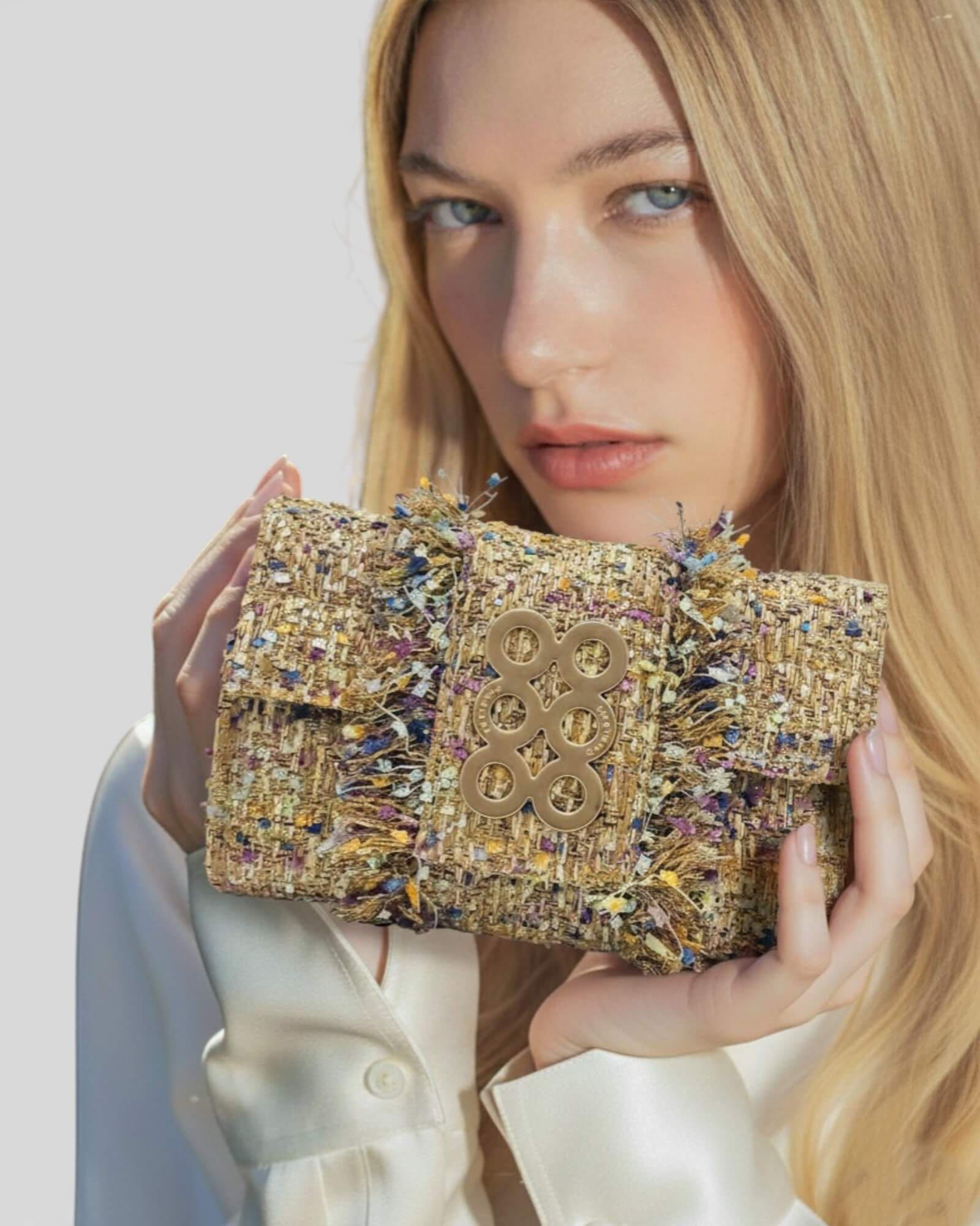 Modelo sosteniendo un bolso de hombro Kooreloo de tweed artesanal con acabado deshilachado y herrajes dorados.