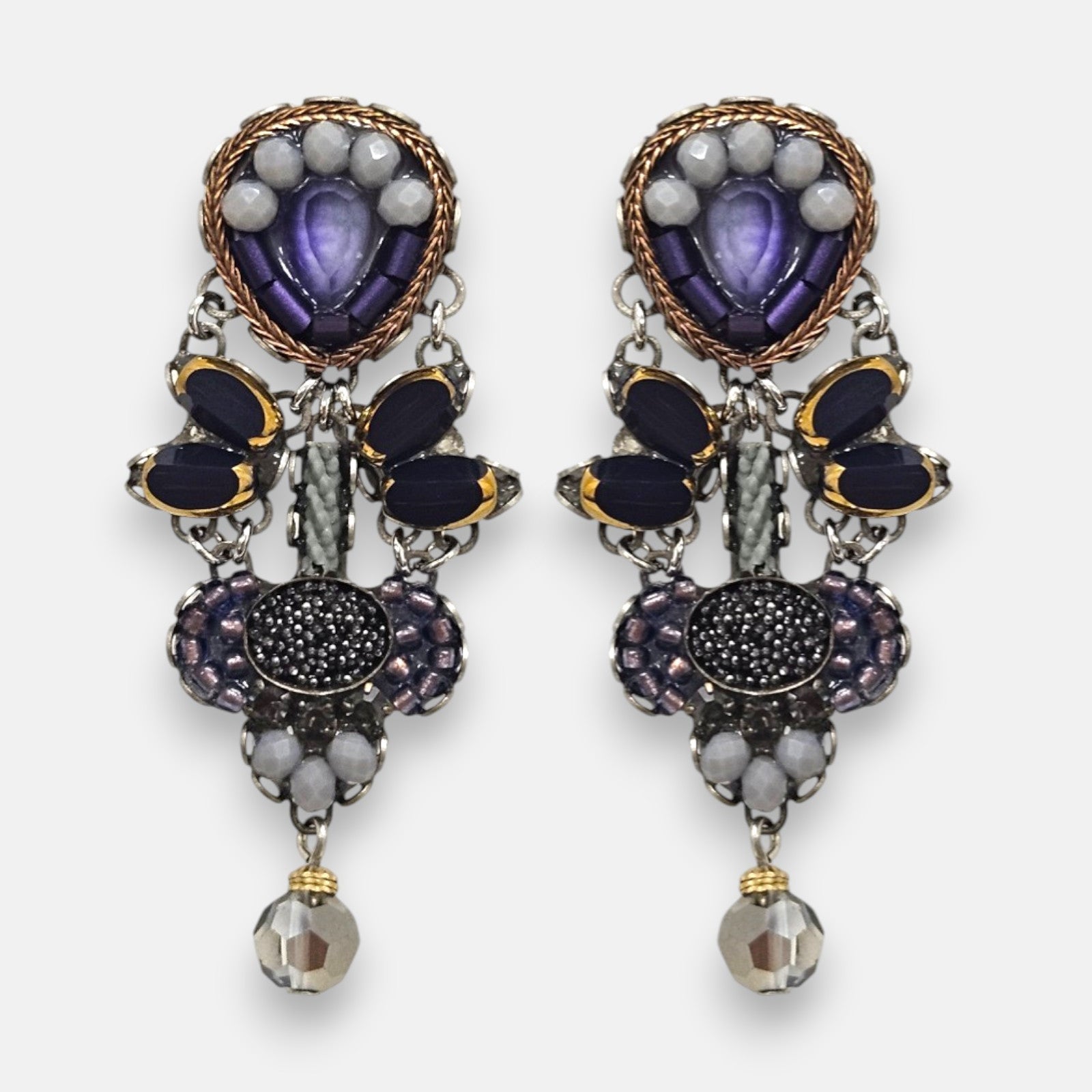 pendientes expuesto de frente sobre fondo claro, detallando su composición simétrica con cristales violetas, negros y cuentas facetadas.