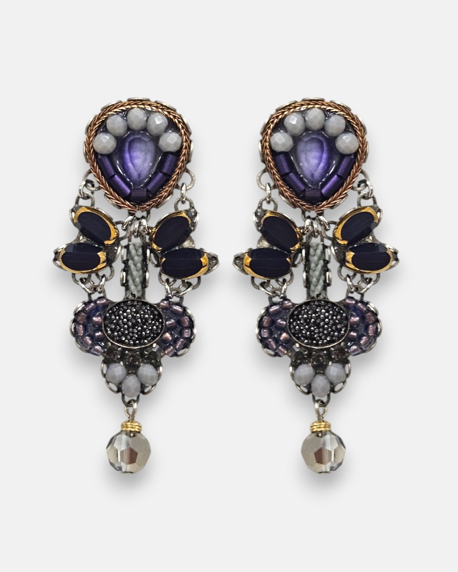 pendientes expuesto de frente sobre fondo claro, detallando su composición simétrica con cristales violetas, negros y cuentas facetadas.