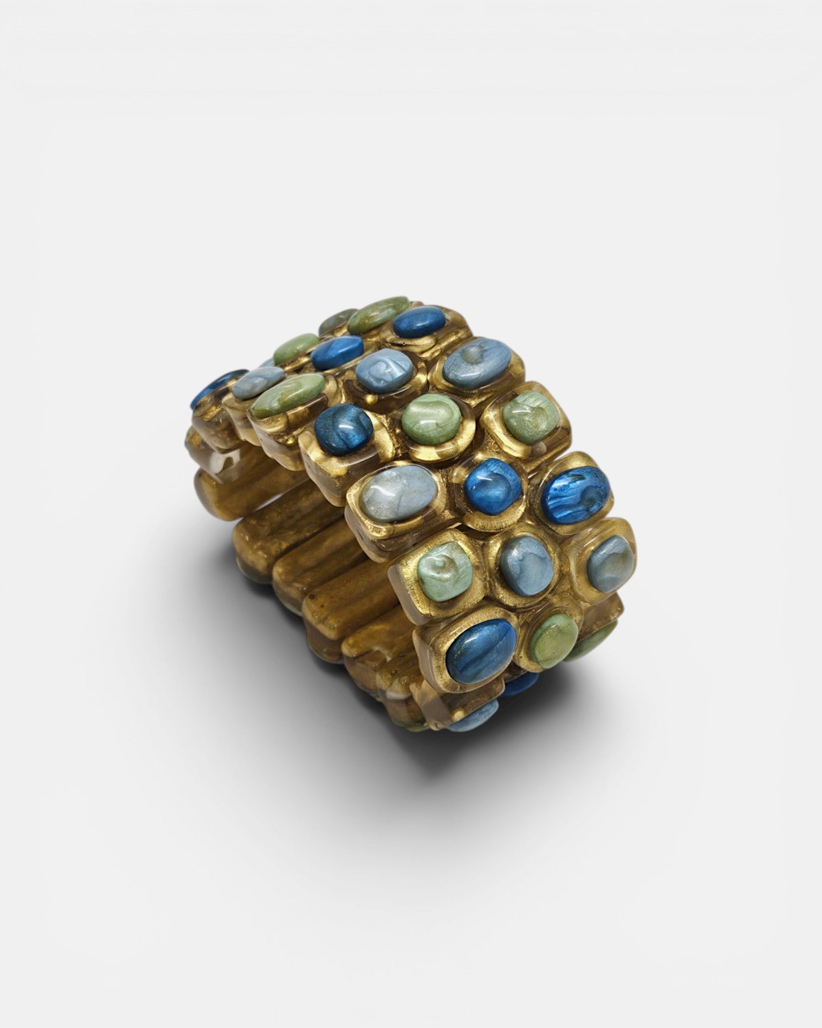 Brazalete ancho Teria de Dominique Denaive mostrando sus tres filas de cabujones en tonos azules y verdes sobre fondo blanco.